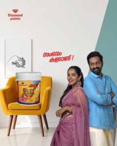A No 1 Paint Company in India—Diamond Paints ad showing a smiling man and woman next to a yellow chair holding a bucket of Dia-Bond Bonding Primer. The red Malayalam text 'സംഭവം കളറാണ്!' is in the center.